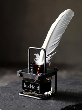 A glass inkwell labelled InkHold, with a white quill resting in it